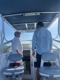 Two individuals converse at the helm of a boat, showcasing the interior seating and controls — ideal for navigating the open waters.