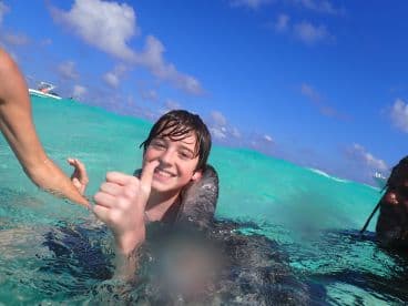 A joyful child gives a thumbs up while swimming with a friendly sea creature in crystal-clear waters — a memorable wildlife encounter in a tropical paradise.