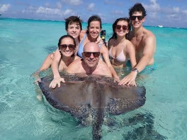 A joyful group interacts with a stingray in shallow waters, creating unforgettable memories during their aquatic adventure.