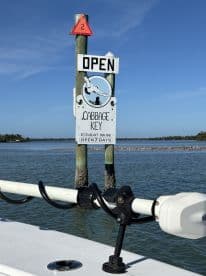 A sign indicating that Cabbage Key is open for business, featuring a scenic view of the water and surrounding area.