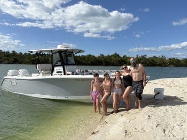A joyful family poses on the beach next to their boat, enjoying a sunny day by the water — perfect for summer adventures and family outings.