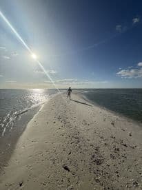A person walks along a sandy strip of beach under the sun, capturing the serene beauty of a tropical island setting — perfect for beach lovers and adventure seekers.