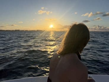 A child gazes at a stunning sunset from the deck of a boat, capturing a serene moment on the water — perfect for family outings and sunset cruises.