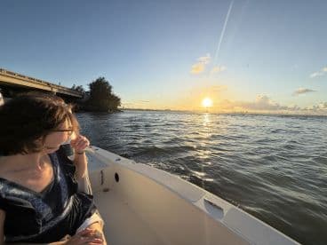 A serene sunset view from a boat, featuring a guest enjoying the moment as the sun sets over the water — perfect for capturing the beauty of evening cruises.