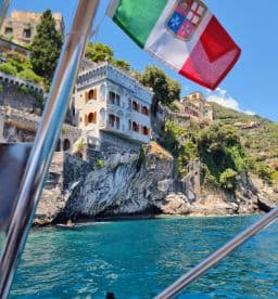 A stunning view of coastal architecture along the Italian coastline, captured from a boat, showcasing the beautiful turquoise waters and vibrant landscape.