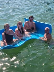A cheerful group enjoys a sunny day floating on a mat in the water, perfect for summer fun and relaxation.