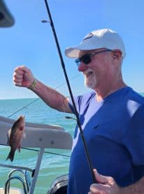 A man proudly displays his catch while fishing on a sunny day at sea, capturing the joy of a successful fishing trip.