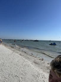 A vibrant beach scene with people enjoying the water and various boats in the background, perfect for a day of fun in the sun.