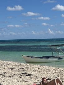 A serene beach scene featuring a small boat anchored nearby, with a sunbather enjoying the tropical sun — perfect for a relaxing day by the water.