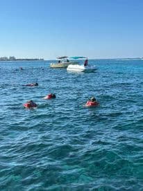 A lively group enjoys snorkeling in clear waters, with boats anchored nearby, creating a perfect setting for aquatic adventures.