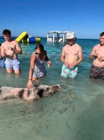 A group of friends interacts with a swimming pig in shallow waters, creating a memorable wildlife experience in the Bahamas.