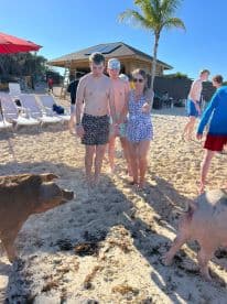 A group of young adults interacts with friendly pigs on the beach, creating a memorable wildlife experience in a tropical setting.