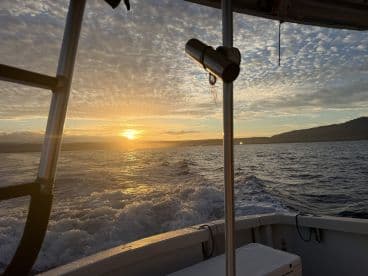 A serene sunset view from the deck of a boat, showcasing the tranquil waters and distant hills — perfect for evening cruises.