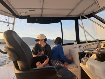 Two young individuals relax inside the helm area of a boat, enjoying the scenic views while seated comfortably. Perfect for family outings or leisurely cruises.