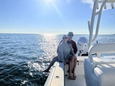 A couple enjoys a sunny day on the water, capturing a romantic moment aboard their boat with sparkling ocean waves in the background.