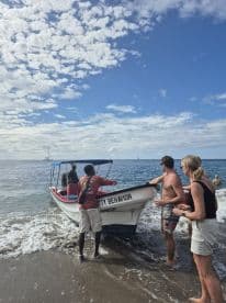 A lively scene at the beach as a group assists with a boat, creating a fun and engaging atmosphere perfect for adventure seekers.