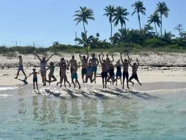 A joyful group of friends and family jumps in celebration on the beach, capturing the essence of fun and togetherness during their tropical getaway.
