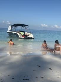 Children play in the shallow waters of a beautiful beach while a boat is anchored nearby, capturing a perfect family day on the water.