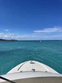 A stunning view from the front of a boat cruising through crystal-clear turquoise waters, showcasing the beauty of the open sea and a distant sailboat.
