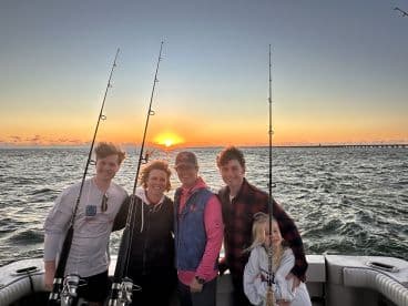 A joyful family poses for a photo while fishing at sunset, capturing a memorable moment on the water. Perfect for family fishing trips and sunset cruises.