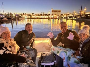 A cheerful group enjoys a cozy evening on a boat, surrounded by festive lights and drinks, perfect for a memorable night out on the water.