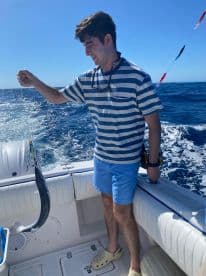 A young man joyfully holds up his catch while fishing on a boat, showcasing the thrill of ocean adventures and the excitement of reeling in a fish.