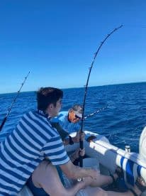 A group enjoys a fishing adventure on the open water, showcasing the excitement of reeling in a catch under the clear blue sky.
