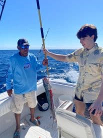 A successful fishing trip captures a moment of excitement as a young man holds up a freshly caught fish alongside an experienced guide, showcasing the thrill of deep-sea fishing in Belize.