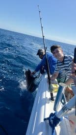 Two anglers celebrate a successful catch while fishing in the open ocean, showcasing the thrill of deep-sea fishing adventures.