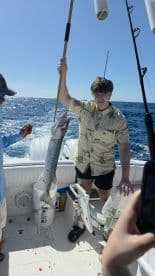 A young angler proudly displays his catch aboard a fishing boat, showcasing the excitement of a successful fishing trip on the open sea.