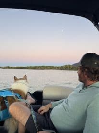 A man enjoys a peaceful moment on a boat with his dog, taking in the serene waters and twilight sky — a perfect snapshot of relaxation on the water.