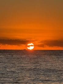 A stunning sunset over the ocean, with a silhouette of a boat on the horizon, creating a picturesque scene perfect for romantic evenings or tranquil boat rides.