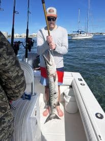 An angler proudly displays a freshly caught barracuda while fishing on a boat, showcasing the thrill of deep-sea fishing adventures.