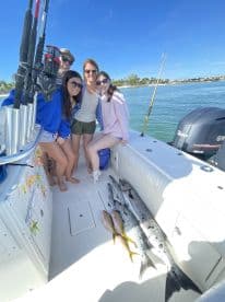 A cheerful group poses on a fishing boat with their catch of the day, celebrating a successful fishing trip in sunny waters.