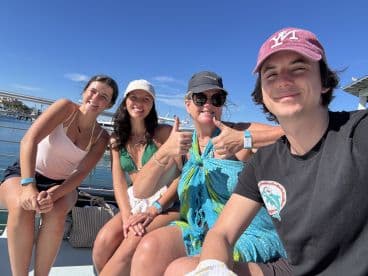 A cheerful group of friends poses for a selfie on a boat, enjoying a sunny day on the water — perfect for memorable outings and adventures.