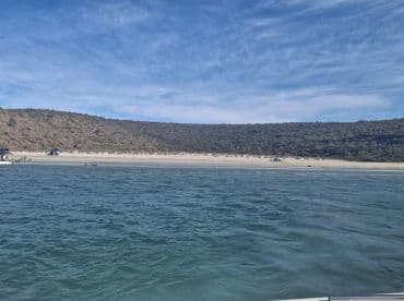 A picturesque view of a serene beach with people enjoying the sun and sand, framed by lush hills — an ideal spot for relaxation and exploration.