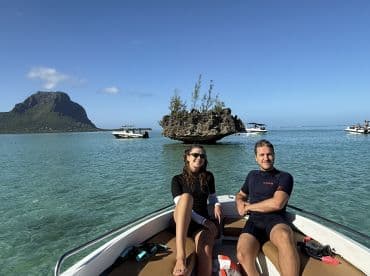 A couple relaxes on a boat in clear turquoise waters, with a stunning island backdrop — perfect for a day of exploration and adventure.