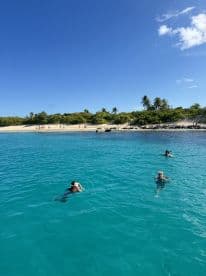 A lively scene of people enjoying a refreshing swim in crystal-clear turquoise waters, with a beautiful beach backdrop — perfect for a fun day in the sun.