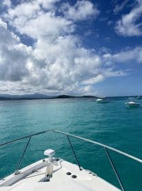 A stunning view from the front of a boat cruising through crystal-clear turquoise waters, with picturesque clouds and distant islands in the background.