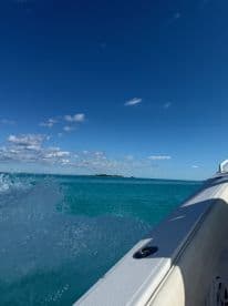 A stunning view from the side of a boat cruising through crystal-clear turquoise waters, showcasing the beauty of the open sea and distant islands.