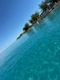 A scenic view of clear turquoise waters with distant trees and docks, creating a serene coastal atmosphere.