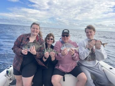 A joyful family displays their catch of the day while fishing on the open ocean, capturing the excitement of a memorable fishing trip together.