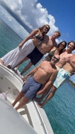 A lively group of friends enjoys a day out on the water, posing on the bow of a boat under a bright blue sky — perfect for summer adventures and memorable moments.