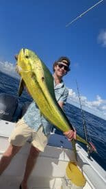 A proud angler holds up a large dolphin fish aboard a fishing boat, showcasing the thrill of deep-sea fishing in the open ocean.