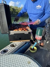 A chef prepares a delicious barbecue on a boat, showcasing a grill filled with various meats — perfect for onboard dining experiences in the Florida Keys.