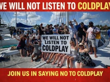 A lively group aboard a boat holds a humorous sign declaring their stance against Coldplay, showcasing a fun and spirited atmosphere perfect for memorable outings.