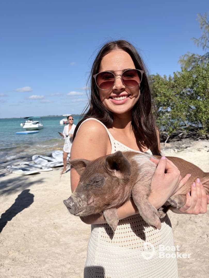 A joyful moment captured as a woman holds a pig on the beach, showcasing a unique human-animal interaction in a picturesque setting.