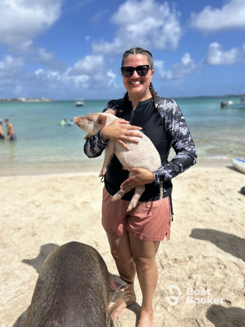 A woman joyfully holds a piglet at a beach, showcasing a unique wildlife interaction — a popular experience in the Bahamas.