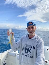 A man proudly holds up his catch while fishing on a boat in the open ocean, showcasing the thrill of a successful day on the water.