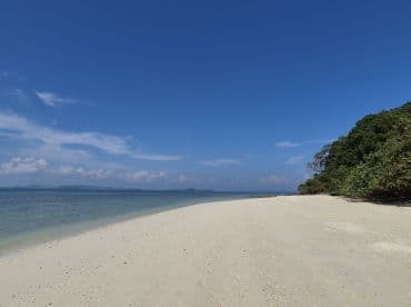 A serene beach scene with soft white sand and clear blue waters, perfect for a relaxing getaway or island exploration.